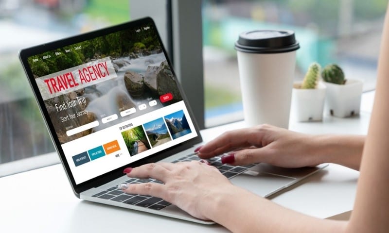 Hands typing on a laptop displaying a travel agency website with a waterfall background